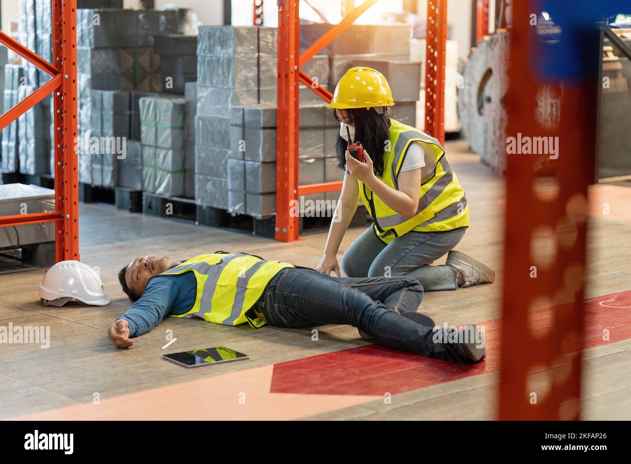 First aid by workmate. Working at warehouse. Male warehouse worker have accident. Stock Photo
