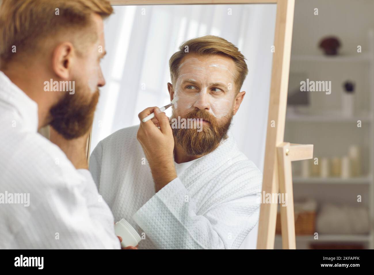 Focused adult man who takes care of skin with brush applies moisturizing anti-aging cream. Stock Photo