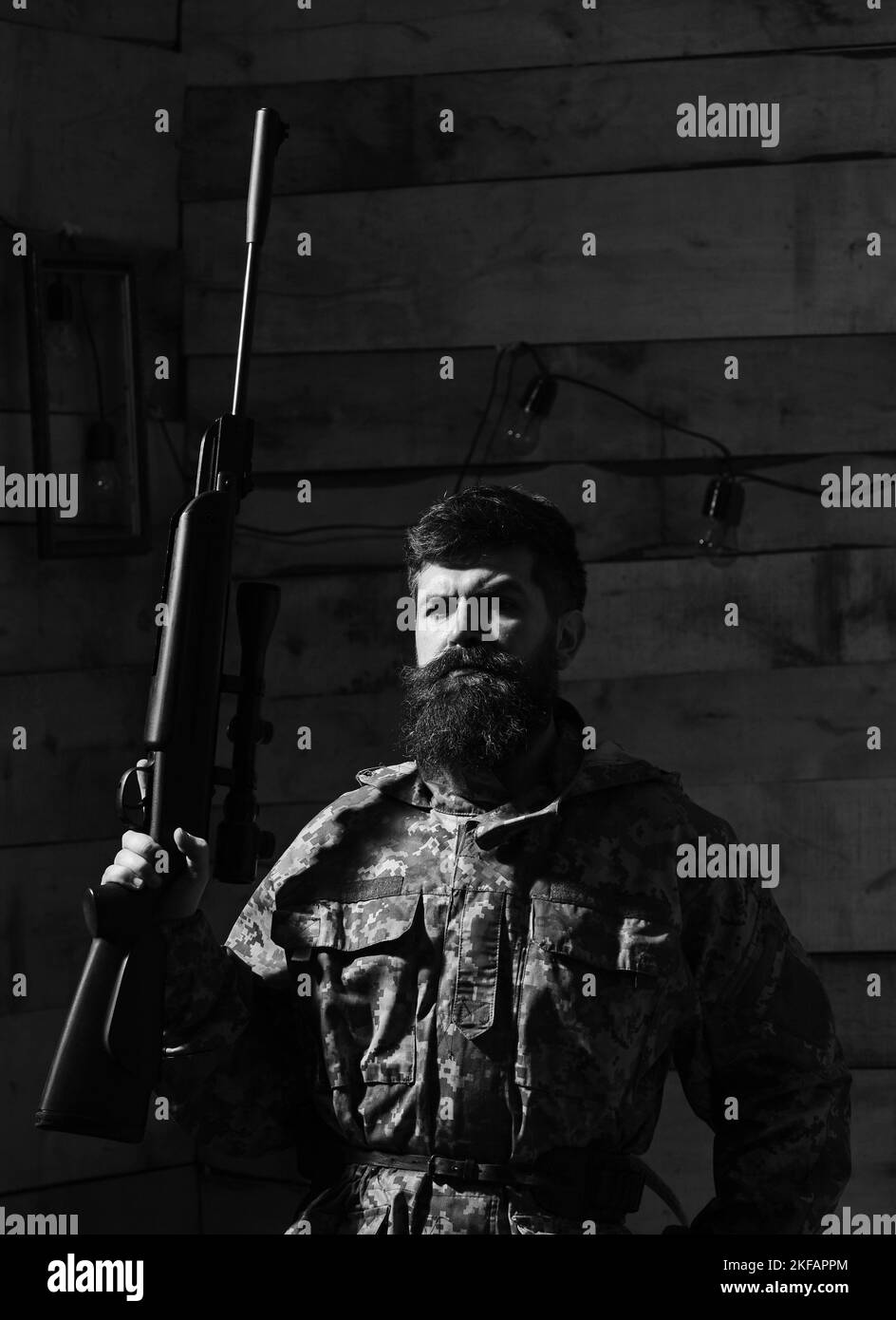 Man with beard wears camouflage clothing, wooden interior background