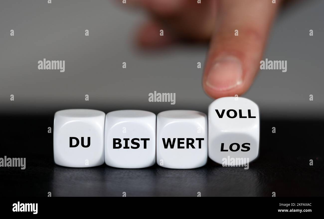 Hand turns dice and changes the German expression 'du bist wertlos' (you are worthless) to 'du bist wertvoll' (you are valuable). Stock Photo