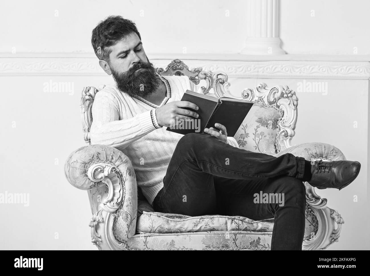 Man with beard and mustache sits on armchair and reading book, white