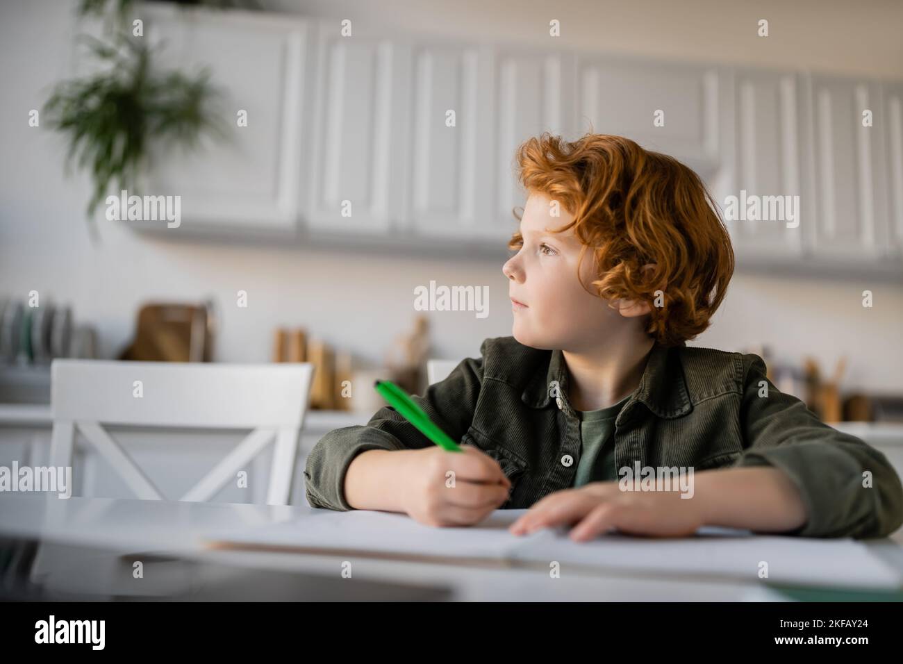 thoughtful redhead boy with pen doing homework and looking away Stock Photo