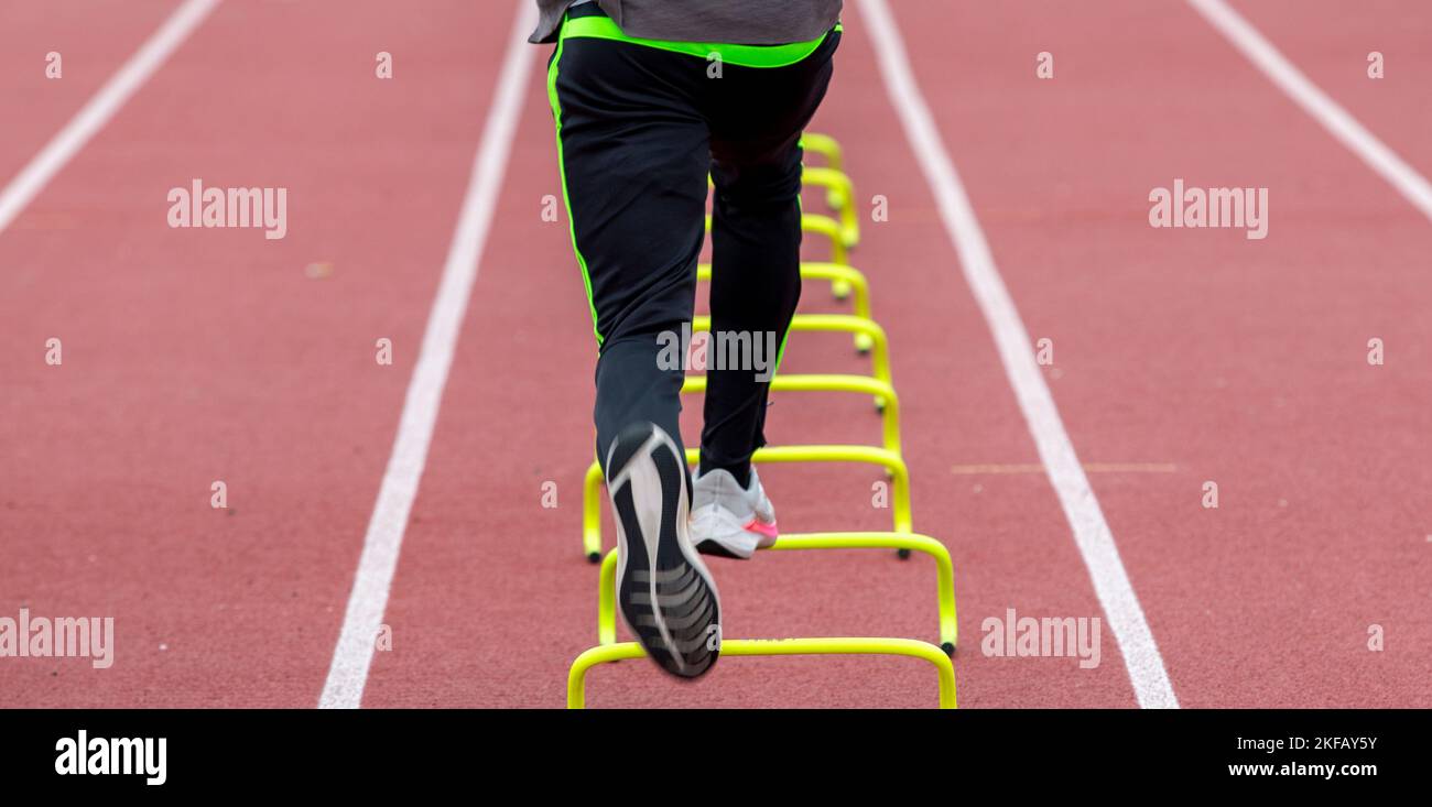 Rear view of a high school runner running over yellow mini hurdles on a