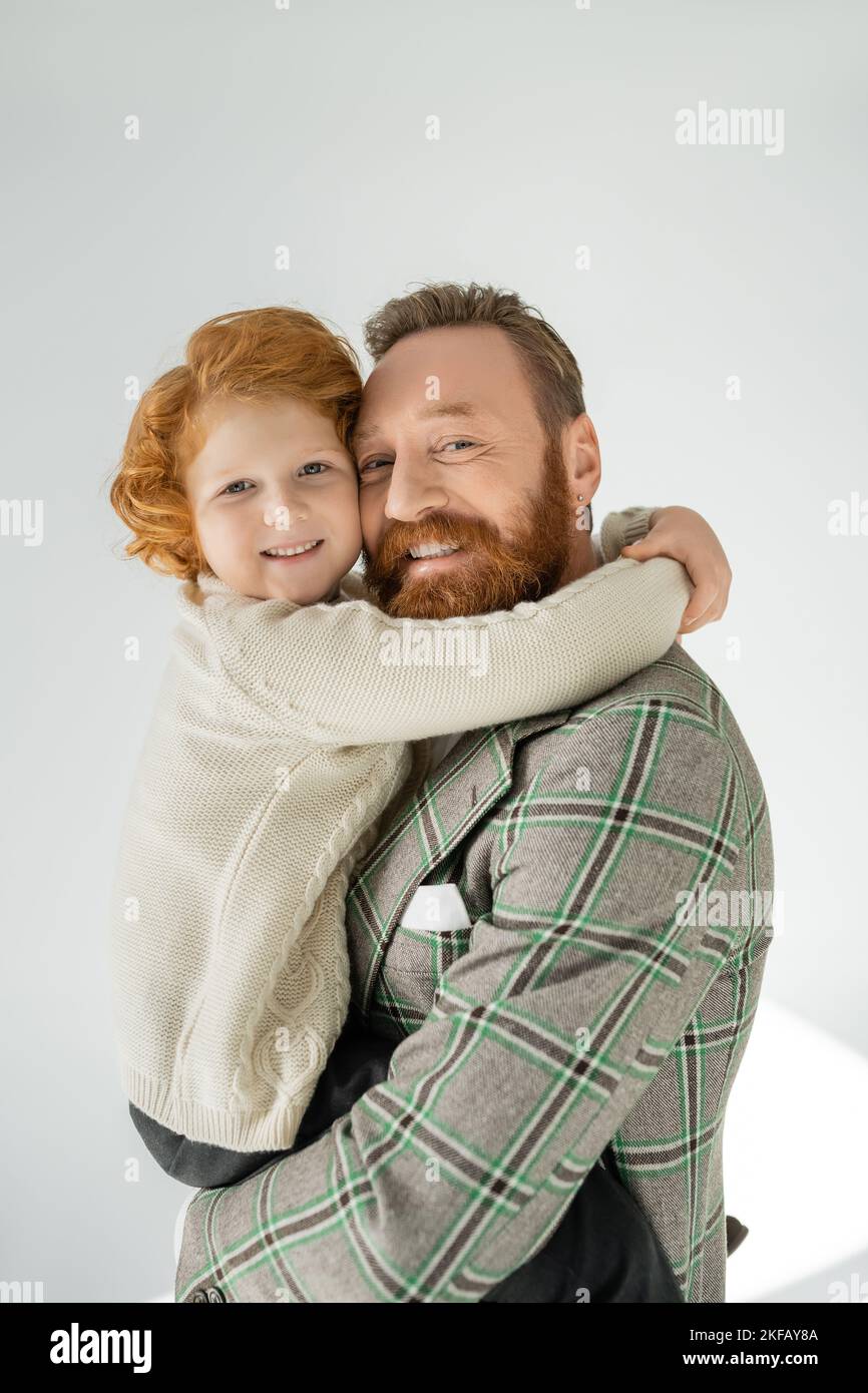 https://c8.alamy.com/comp/2KFAY8A/redhead-boy-in-warm-jumper-embracing-bearded-dad-and-looking-at-camera-on-grey-background-2KFAY8A.jpg
