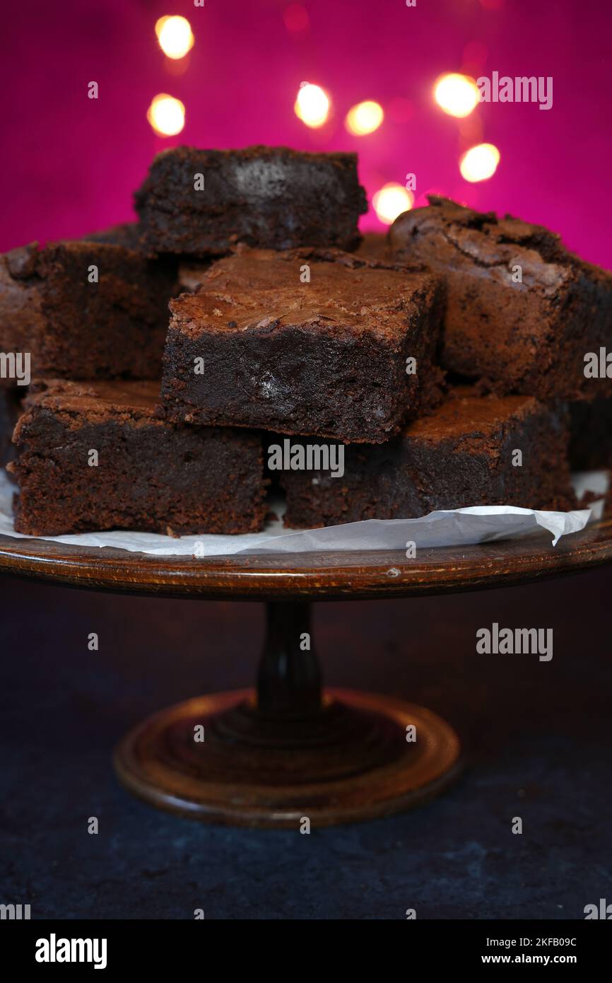 A stack of home baked rich chocolate brownies on a vintage wooden cake