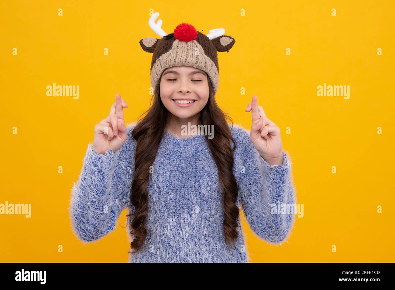 Beautiful winter kids portrait. Teenager girl posing with winter sweater and knit hat on yellow background. Stock Photo