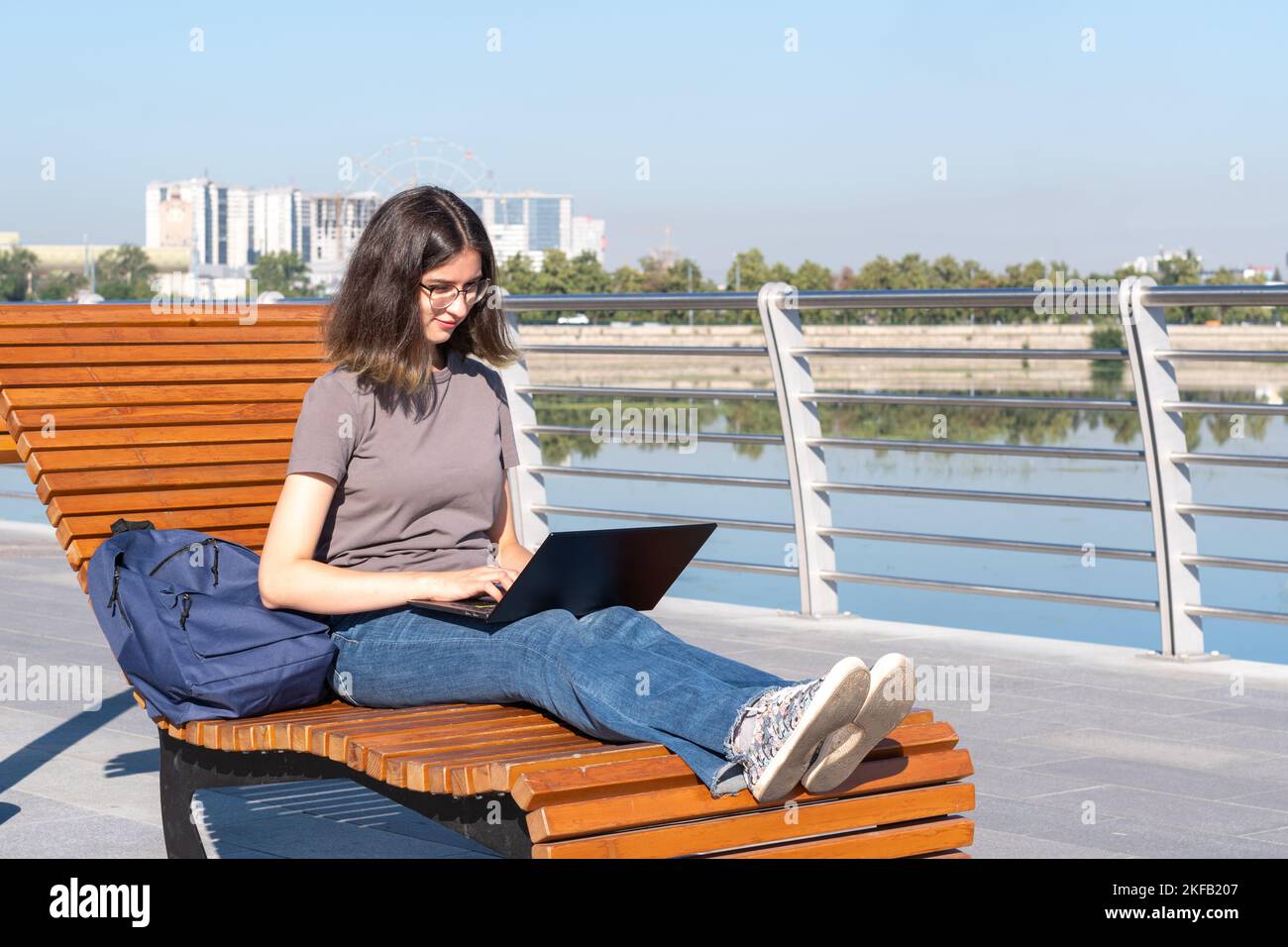 A Spanish student girl with glasses typing text on a laptop, looking for something on the Internet, chatting online with friends while sitting outdoor Stock Photo