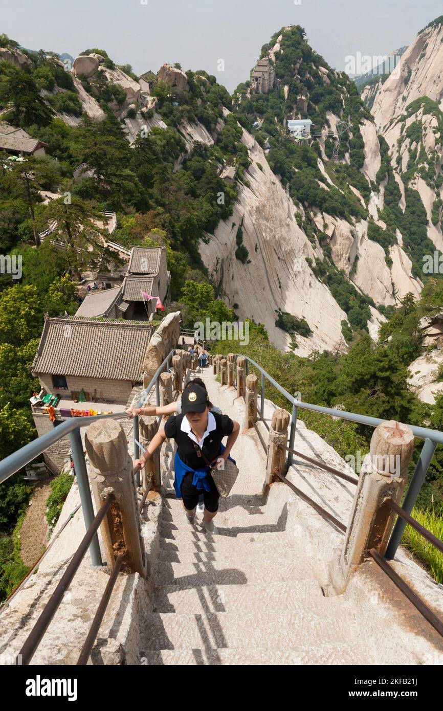 Visitor / tourist climbs steep steps cut into or fixed to a stone rock ridge leading towards a peak / one of the five peaks of Huashan Mountain / Mount Hua / Mt Hua near Huayin, Weinan, China, PRC. (125) Stock Photo