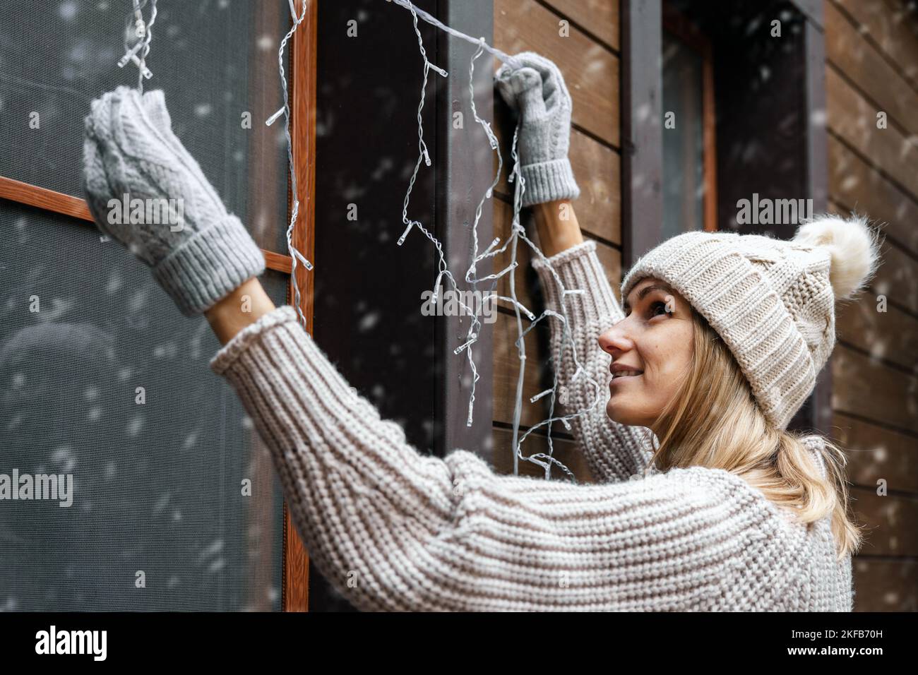 holiday decorations. woman install electric christmas string lights on house exterior facade Stock Photo