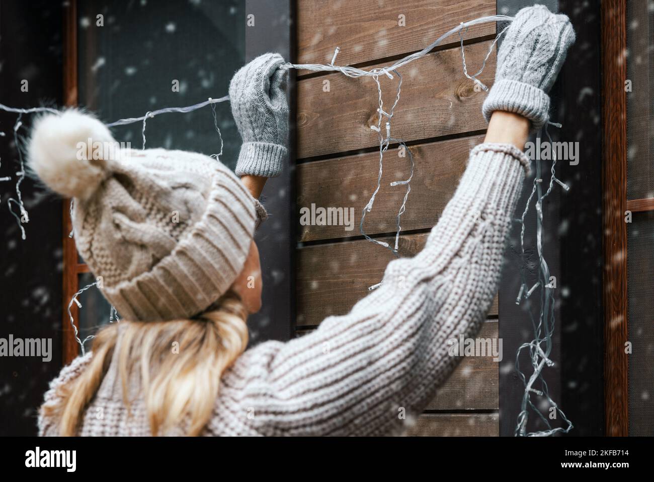 christmas home decorations. woman install electric string lights on house exterior facade Stock Photo