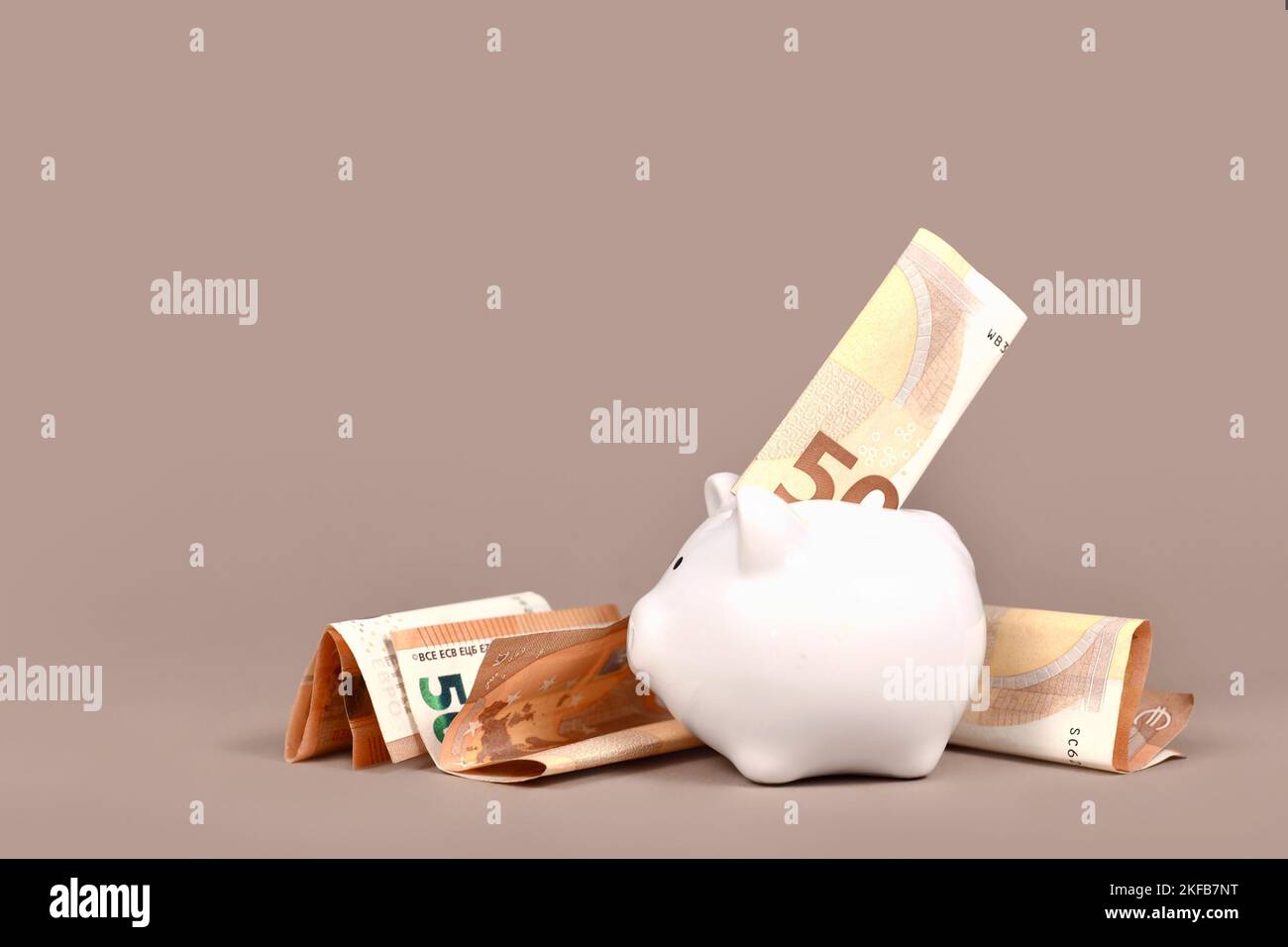 White piggy bank with 50 Euro bills on beige background with copy space. Concept for saving money Stock Photo