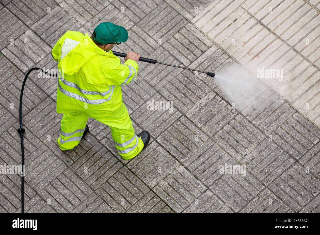 Worker cleaning a pavement sidewalk with high pressure water jet