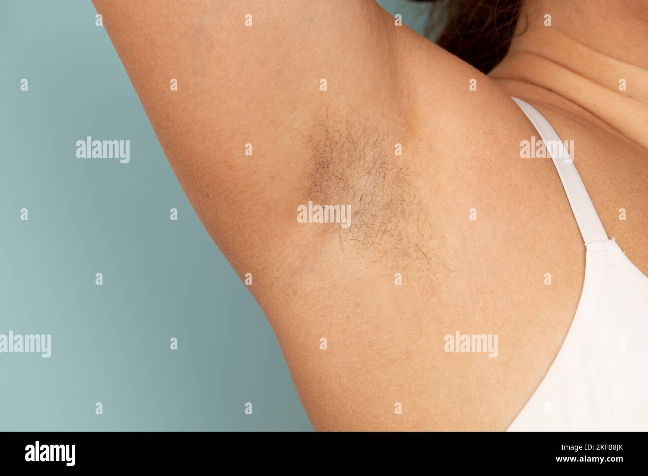 Woman touch hairy underarms with hand closeup, free copy space, yellow background. Raised arm with armpit hair. Female beauty trend, freedom, feminism Stock Photo