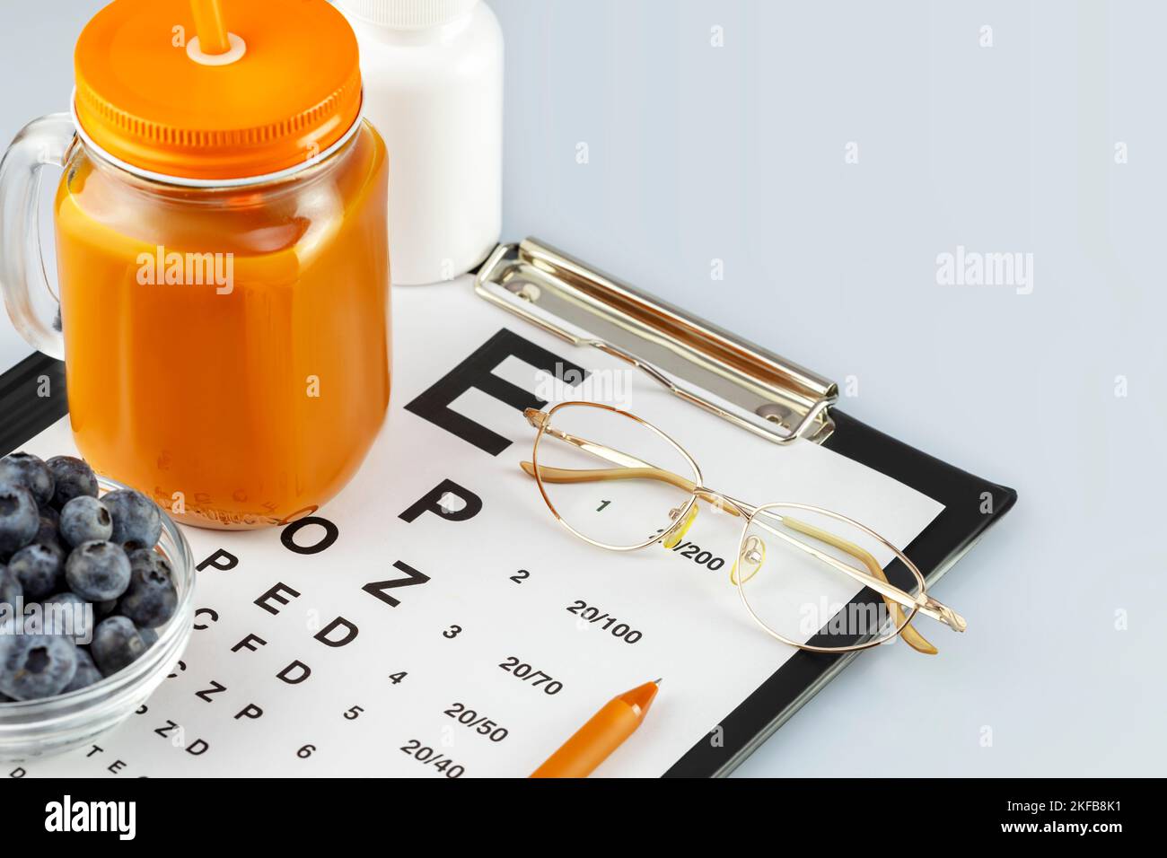 Eyeglasses, glass of carrot juice, bowl with blueberries, vitamins and