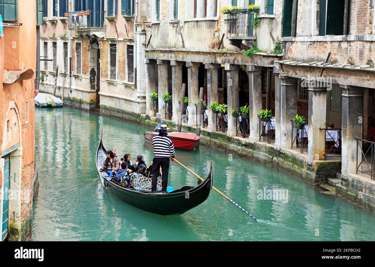 Venice, Italy. Gondoliere steering a gondola with tourists in a narrow canal surrounded by old buildings Stock Photo