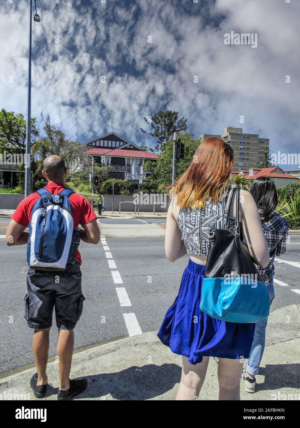 Group of young people, including girl with beautiful red hair wait at crosswalk on windy summer day near Brisbane Australia Stock Photo