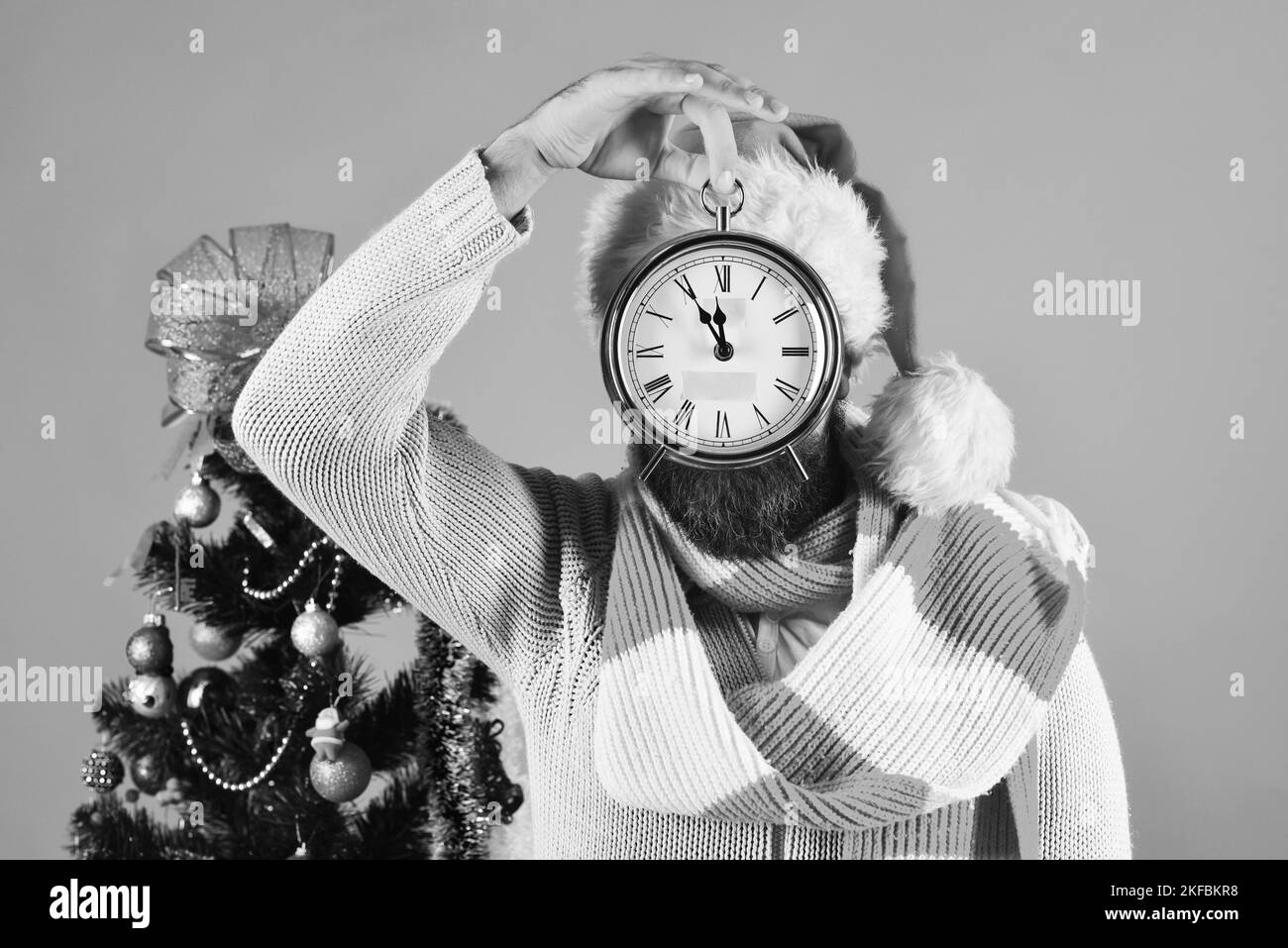 Santa with clock near decorated fir tree. Man with beard Stock Photo