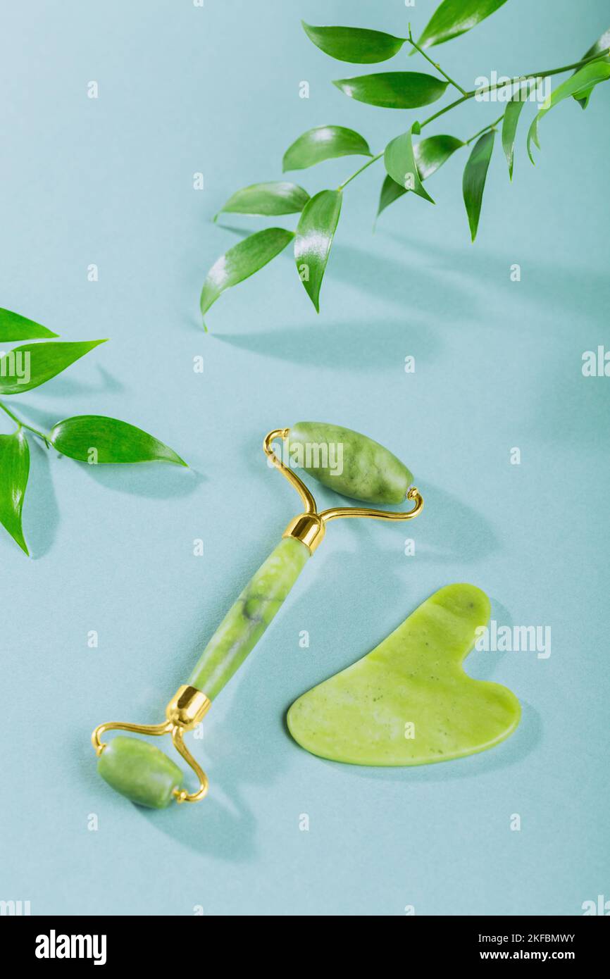 Green jade face roller and gua sha scraper with leaves on light blue