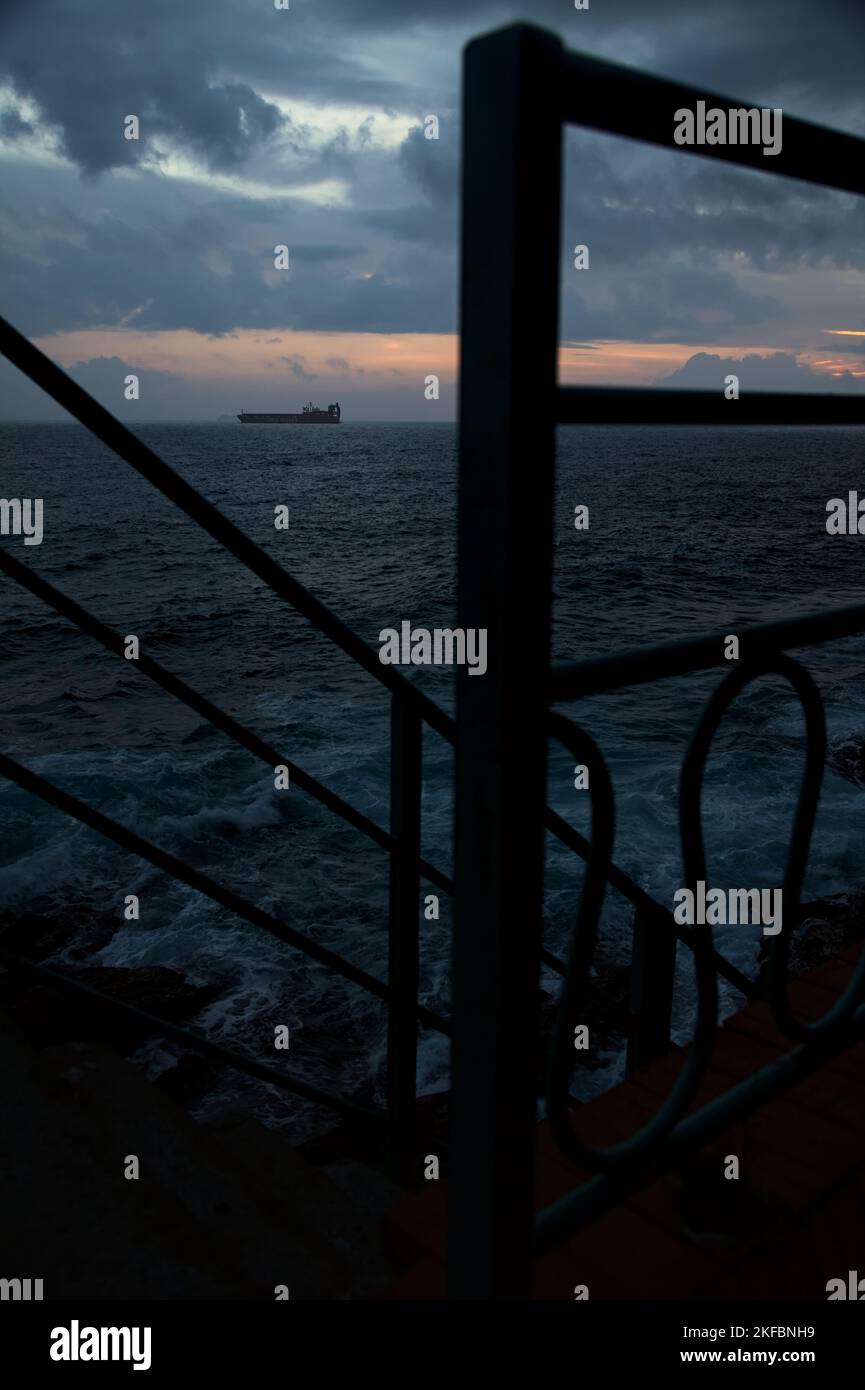 Sea on cloudy day at dusk with a cargo ship in the distance framed by a ...