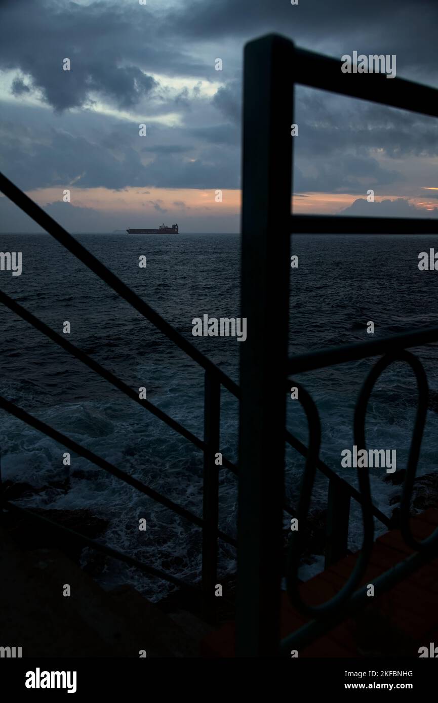 Sea on cloudy day at dusk with a cargo ship in the distance framed by a ...