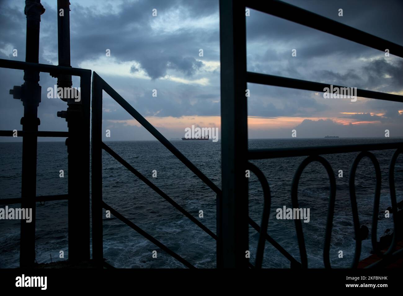 Sea on cloudy day at dusk with a cargo ship in the distance framed by a ...