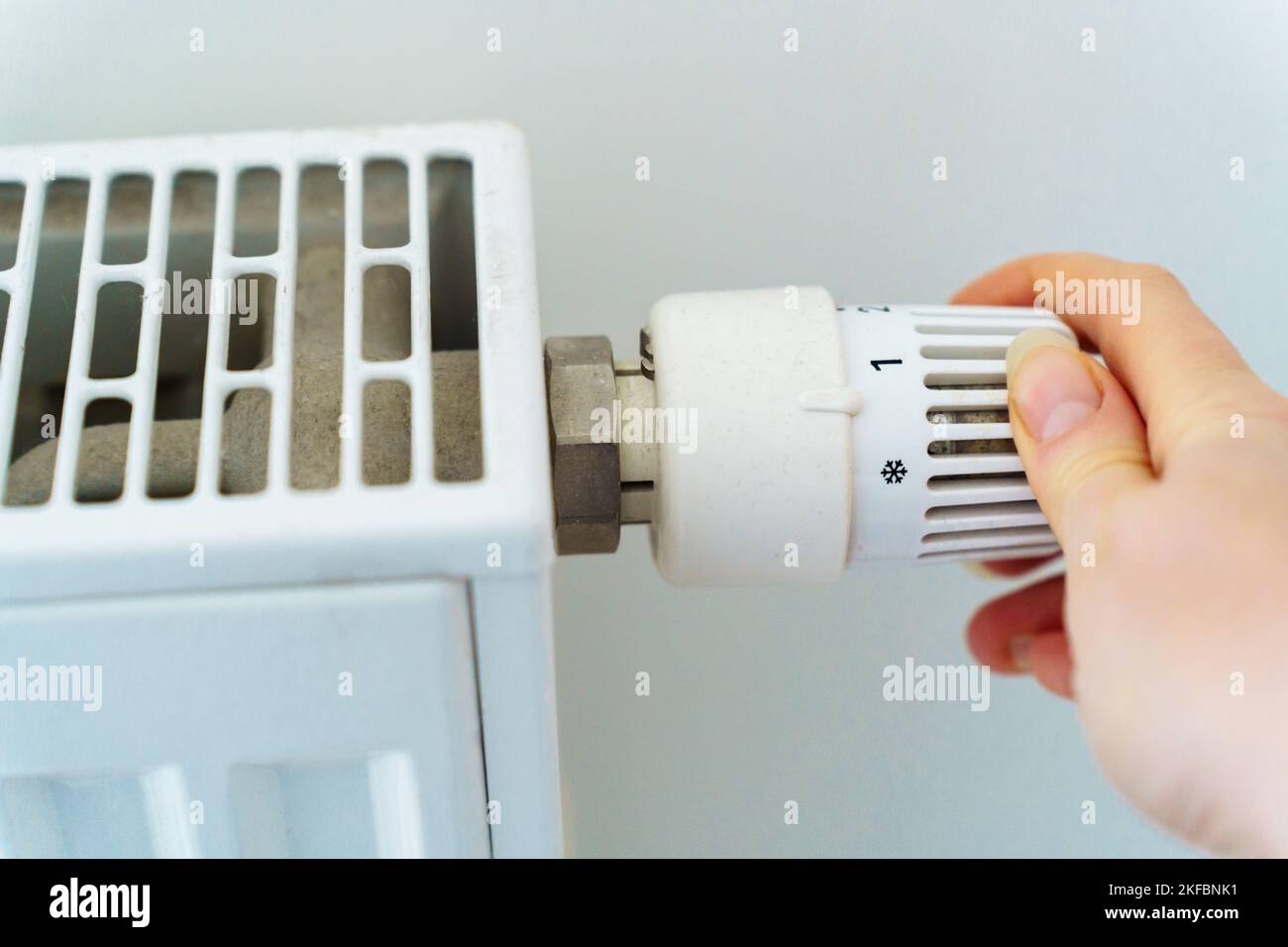 A woman's hand switches the radiator heating regulator to a minimum to save heat energy due to rising prices for nuts and utilities Stock Photo