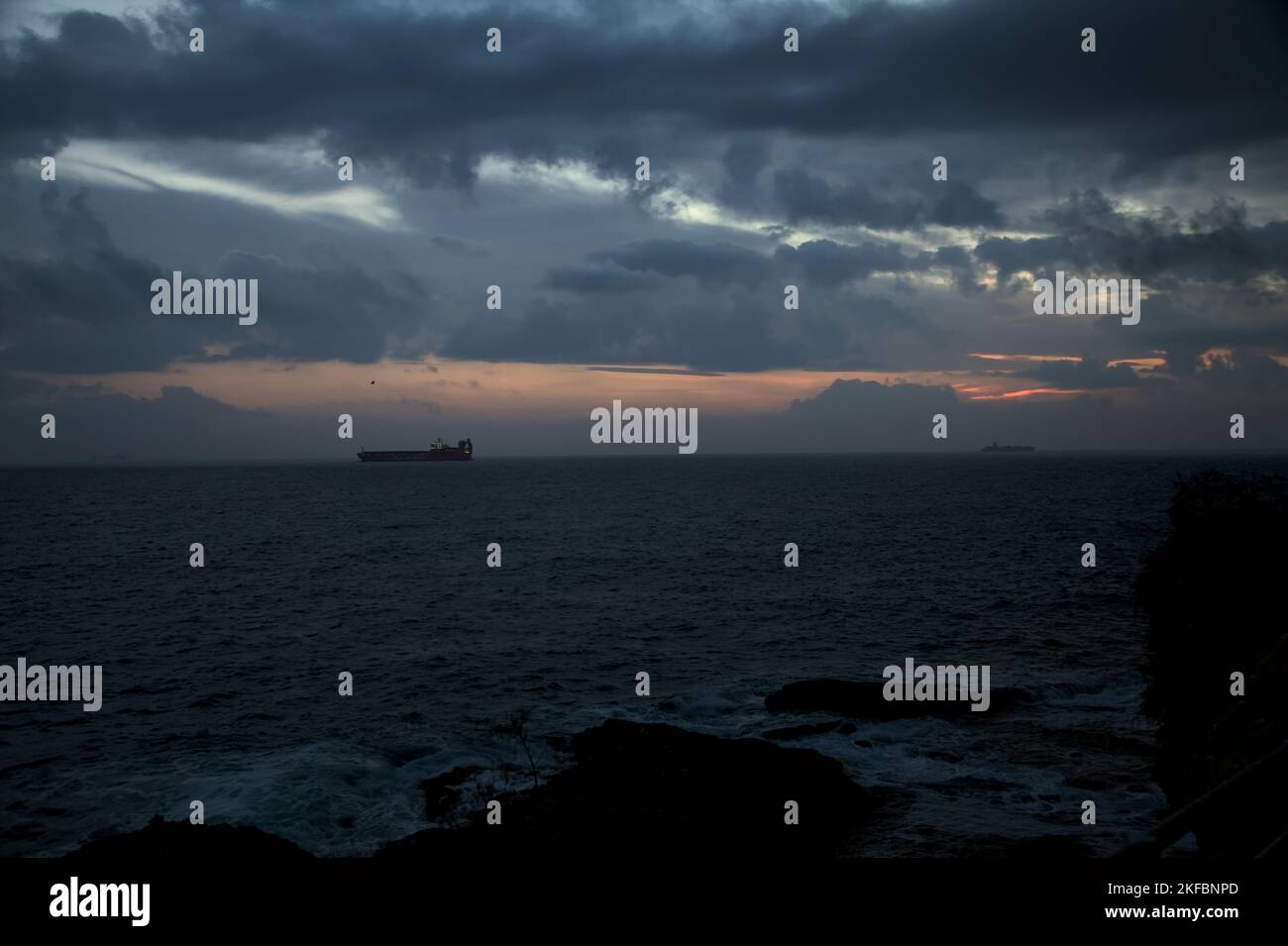 Sea  on a cloudy day at dusk with a cargo ship on the horizon Stock Photo