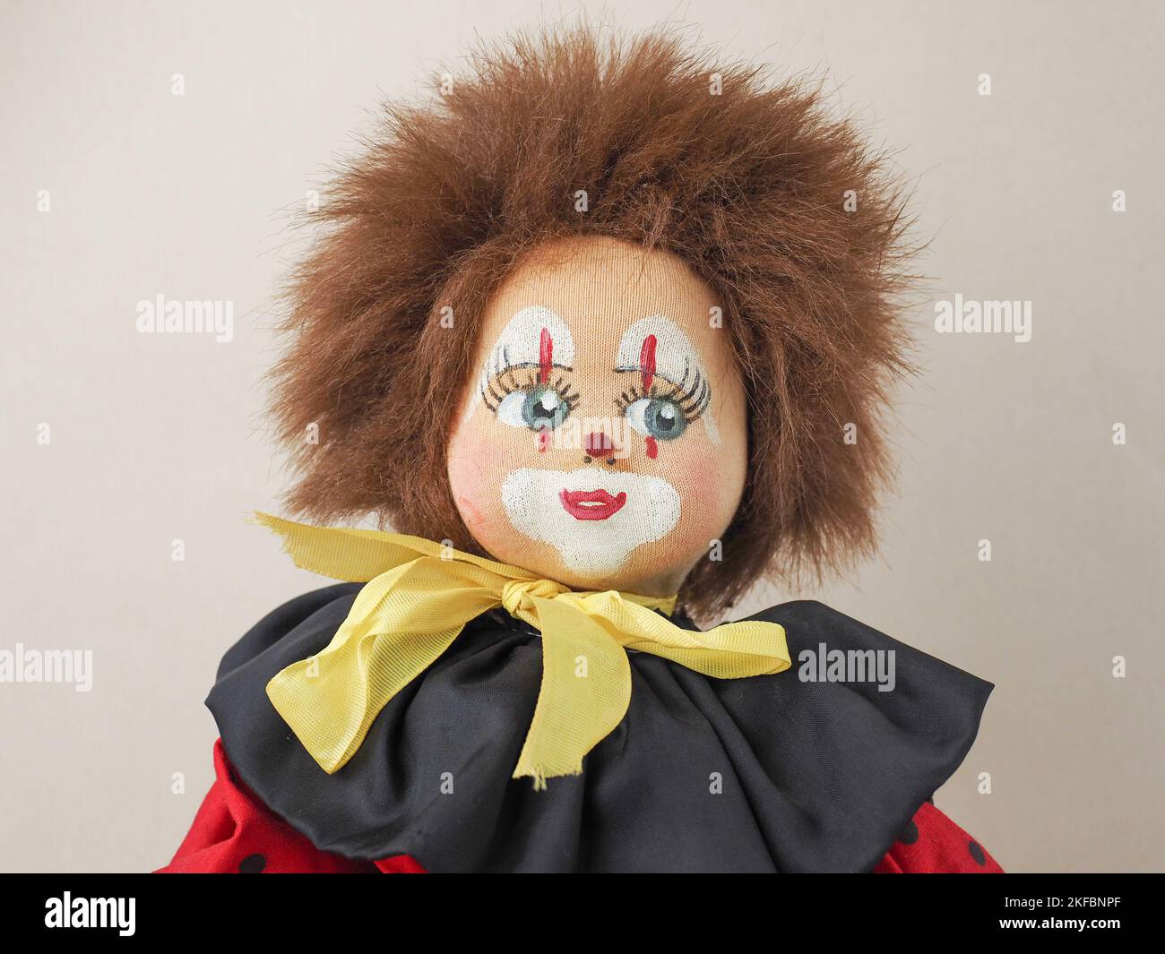 Vintage red-haired clown doll in a red suit with a black collar. Stock Photo