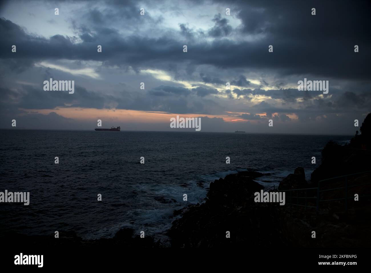 Sea  on a cloudy day at dusk with a cargo ship on the horizon Stock Photo