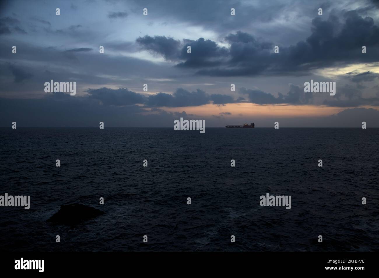 Sea  on a cloudy day at dusk with a cargo ship on the horizon Stock Photo