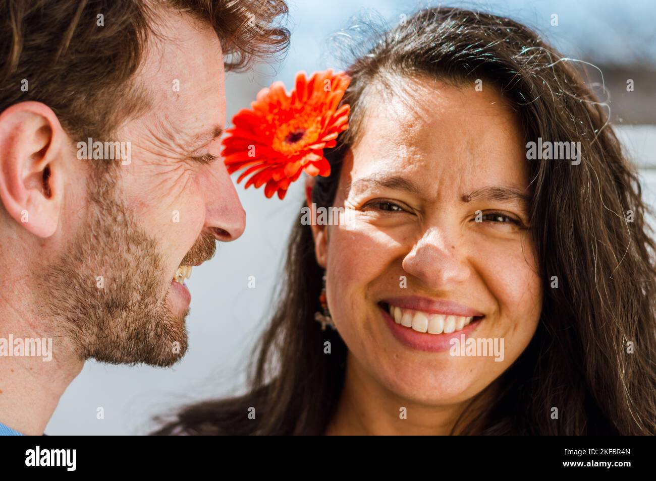 adult latin couple in love at home smiling enjoying the day and playing with flowers, focus on the man who is in profile watching his wife. Stock Photo