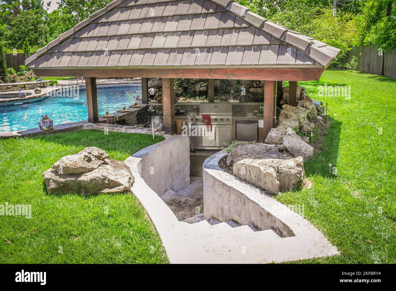 Outdoor kitchen sunken into ground by swimming pool to create a swim-up bar with concrete steps leading down. Stock Photo