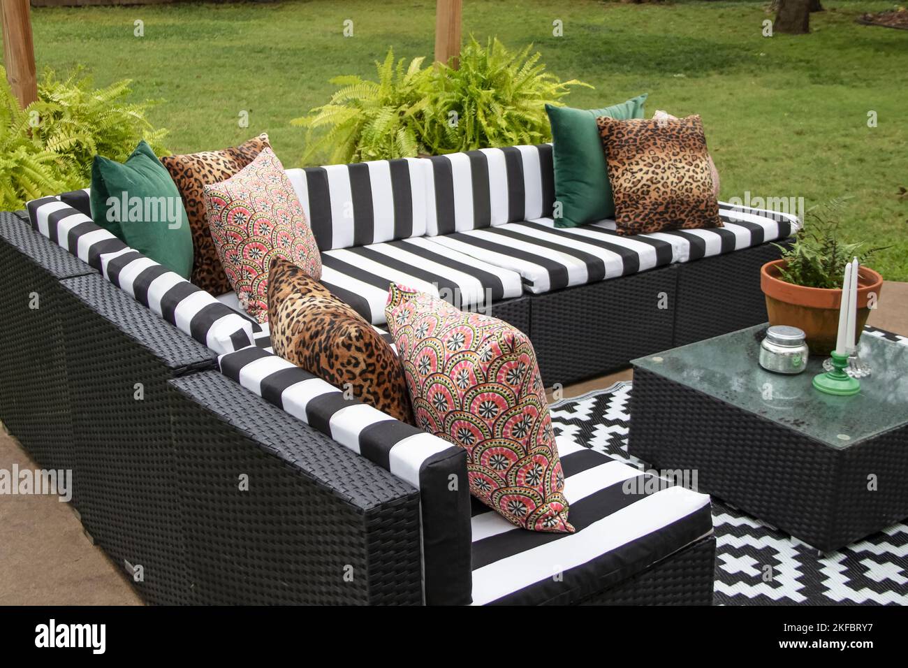 Outdoor lawn furniture with black and white crisply striped upholstery and assorted pillows grouped around a table with ferns on a patio in yard with Stock Photo