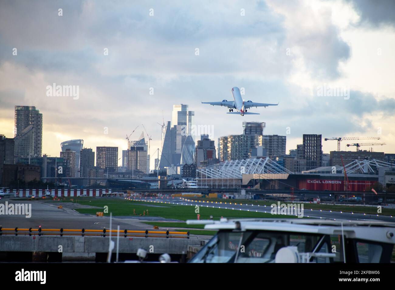 A British Airways Embraer ERJ-190 takes Off into dark clouds at London City Airport with Canary Wharf in the background. Stock Photo