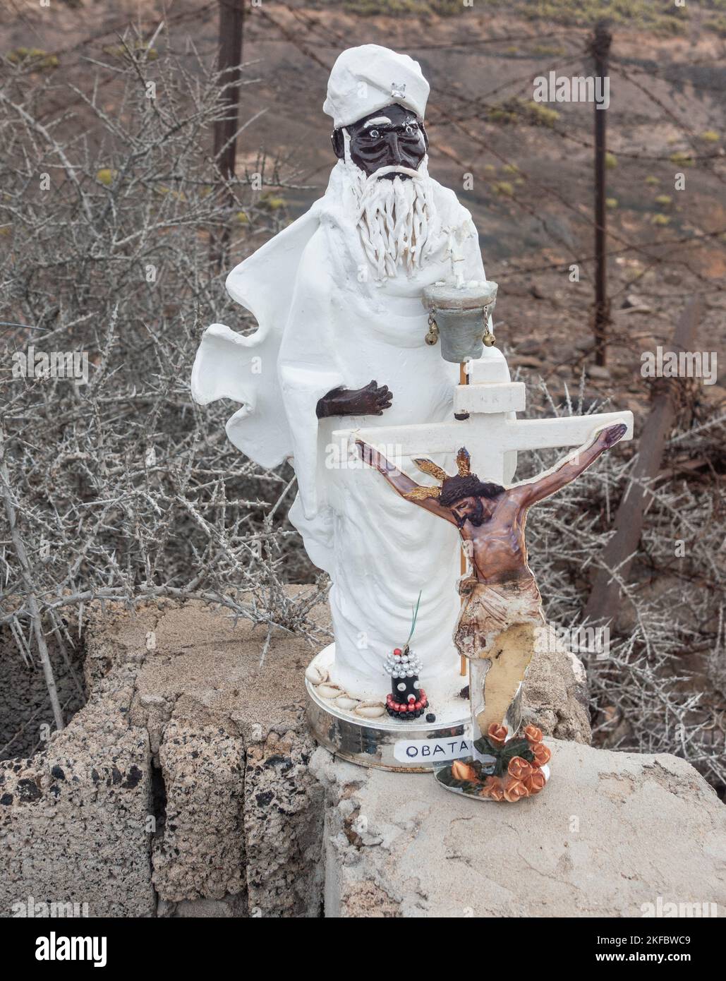 Small statues of Obatala and Jesus Christ on cross by roadside. In the Orisha faiths, Obatalá is the sky father. Stock Photo