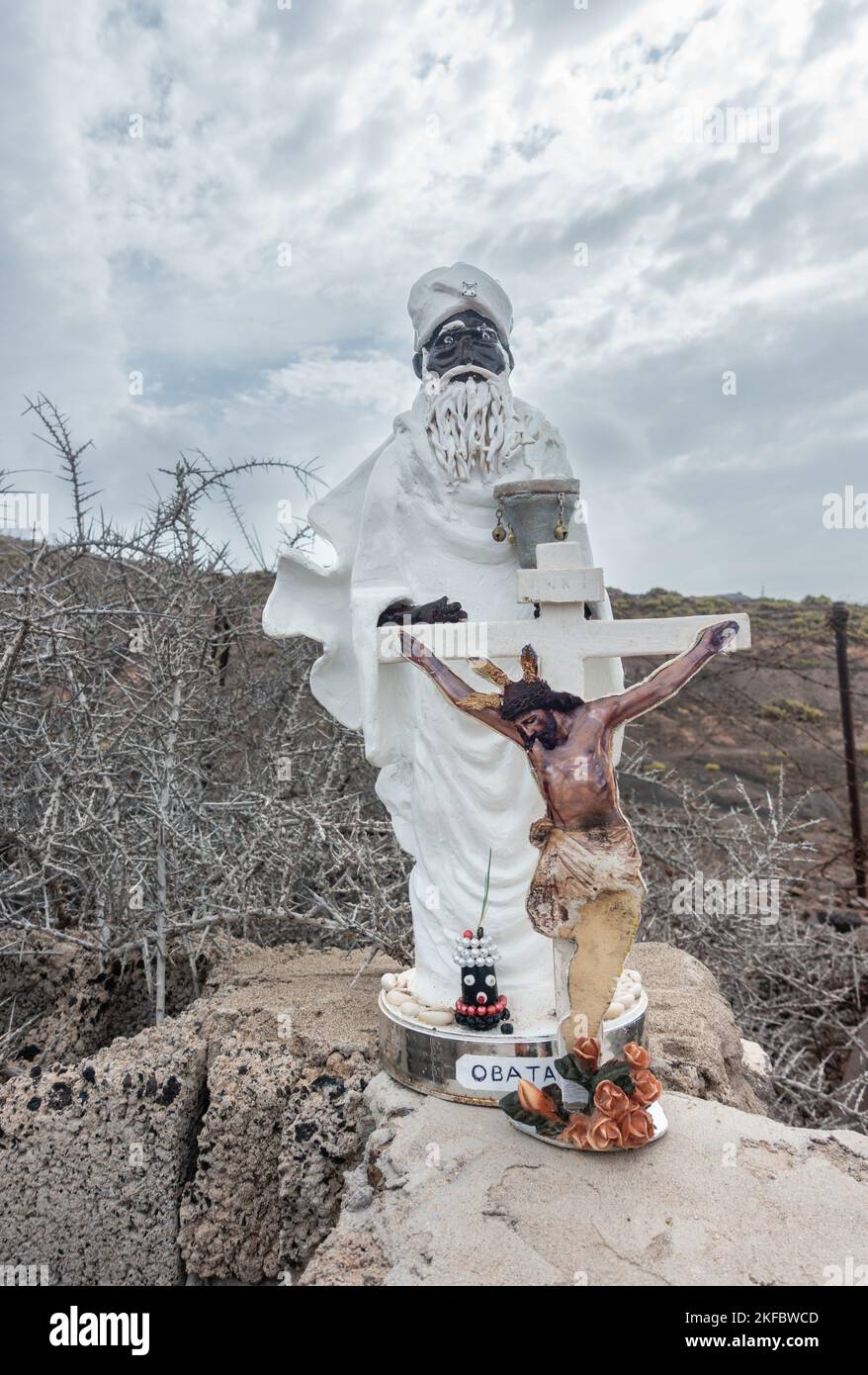 Small statues of Obatala and Jesus Christ on cross by roadside. In the Orisha faiths, Obatalá is the sky father. Stock Photo