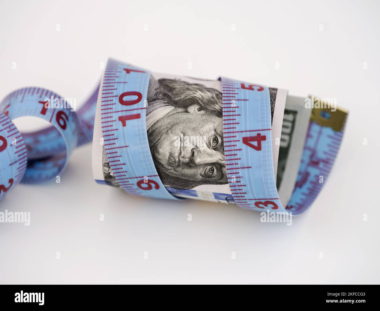 A one hundred dollar bill with a tape measure wrapped around it. Close up. Stock Photo