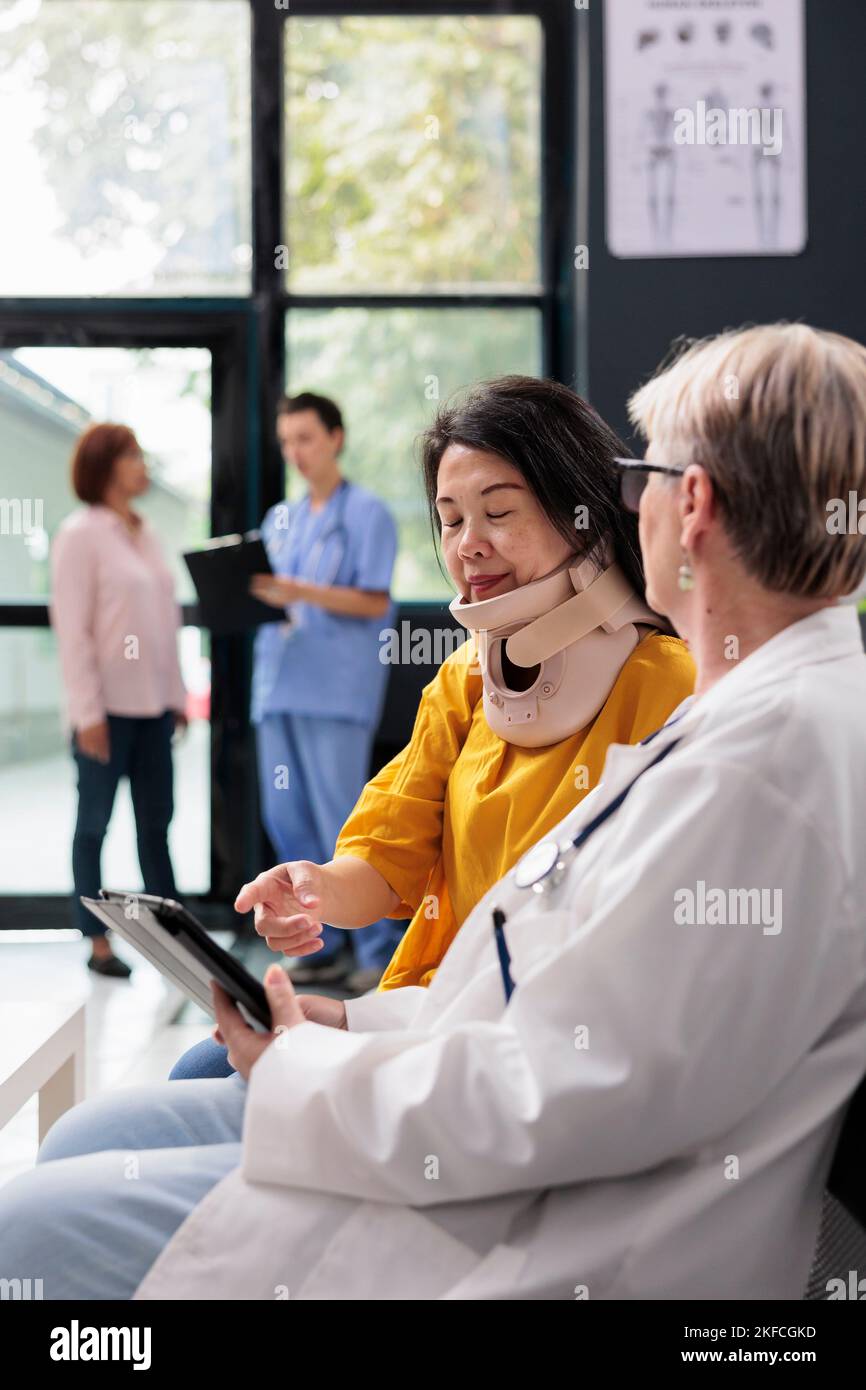 Senior medic consulting patient with cervical neck collar using tablet