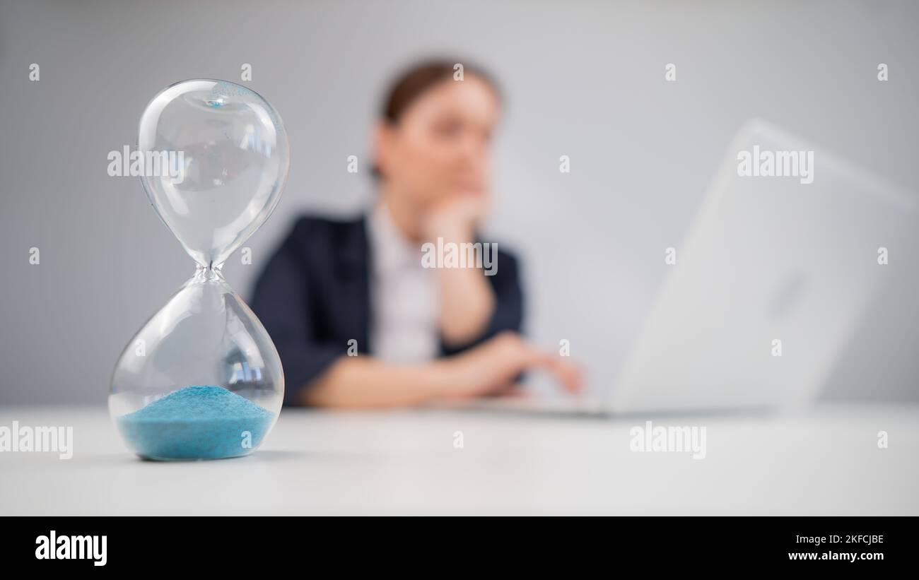 Business woman keeps track of time on an hourglass while working Stock