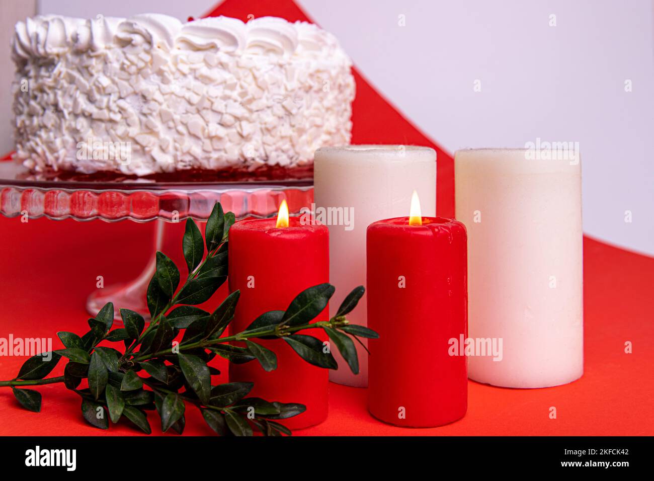 Burning red and white candles on the table. White cake in a glass stand