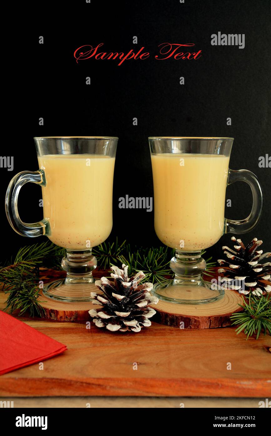 Traditional golden eggnog in tall glass mugs on black background in