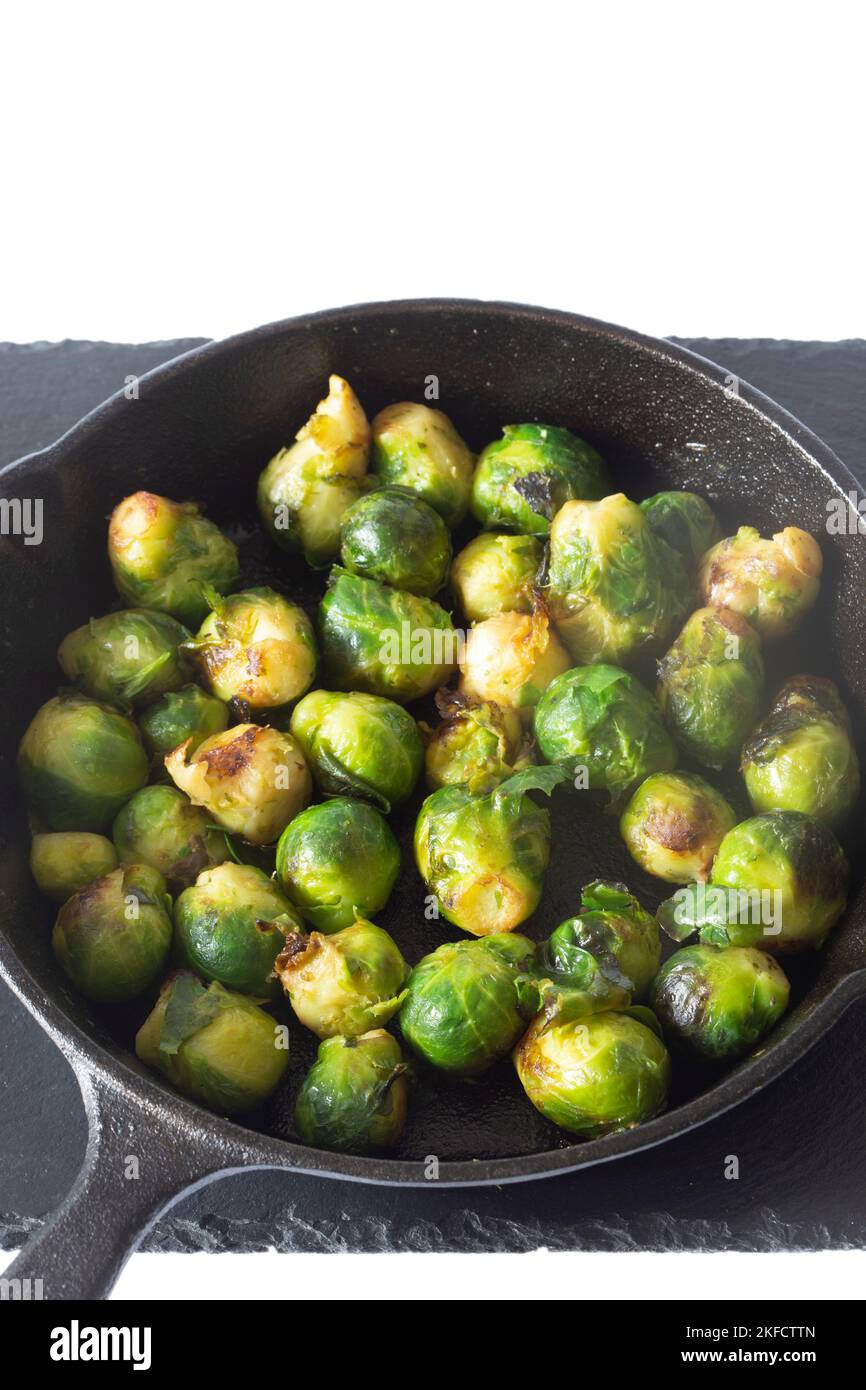Sprouts fried, in a cast iron frying pan with olive oil, on a slate board. Isolated on a white background Stock Photo