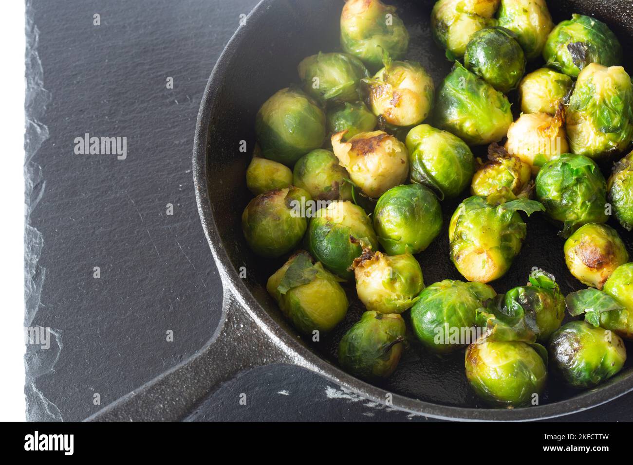 Sprouts fried, in a cast iron frying pan with olive oil, on a slate board. Isolated on a white background Stock Photo