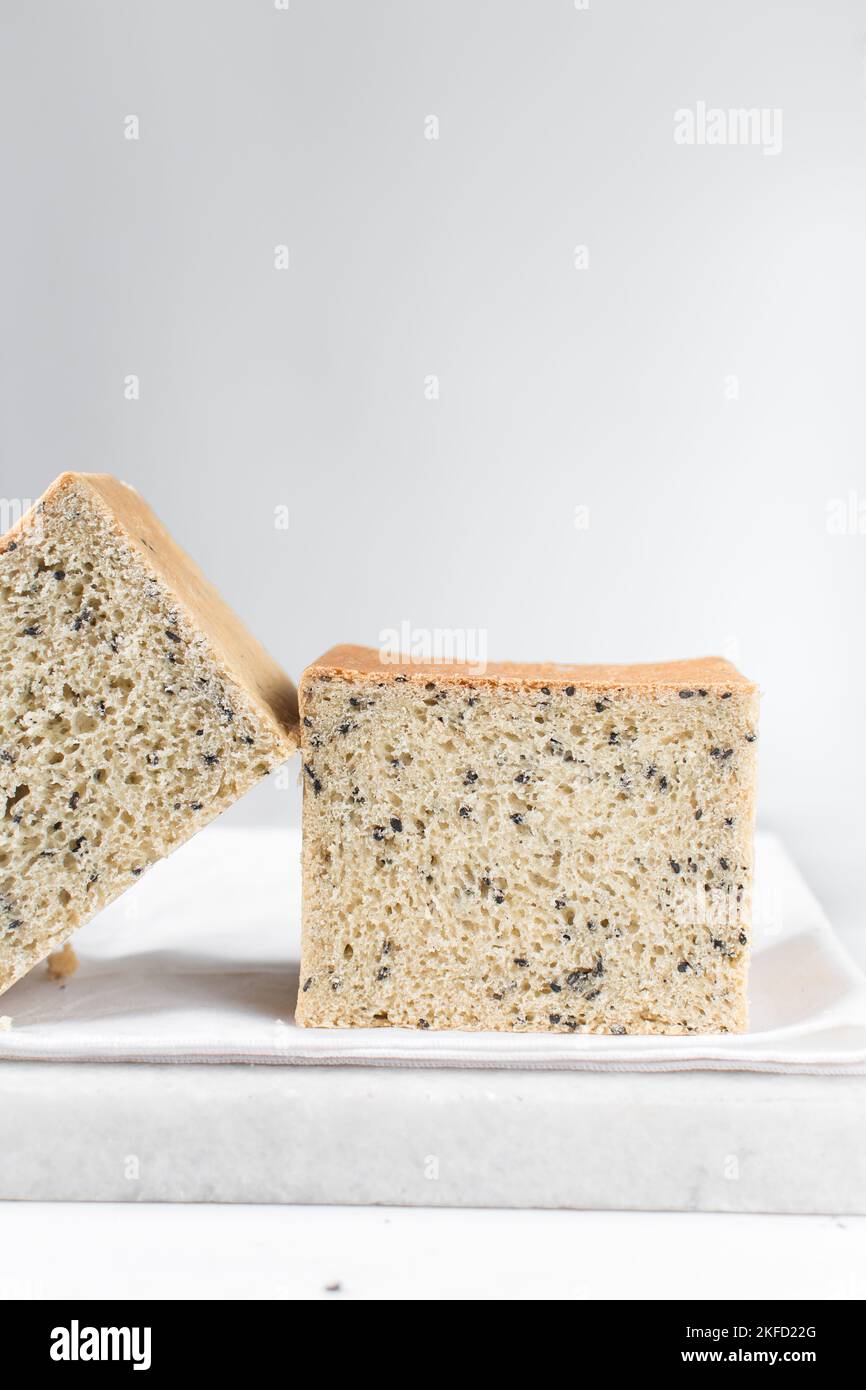 Black sesame seed bread on a white chopping board, poppy seed bread