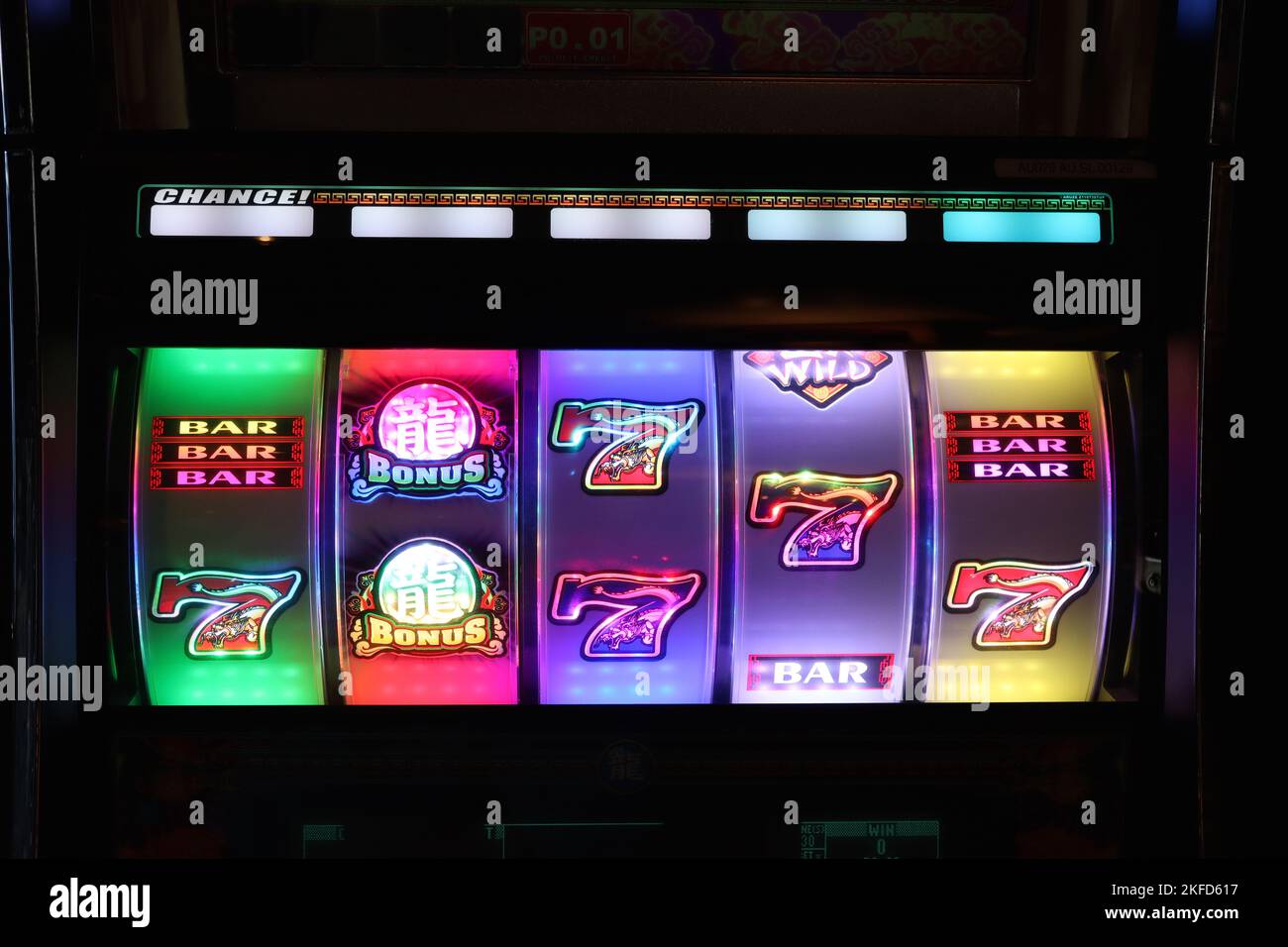 Illuminated slot machine wheels attract players with their colourful graphics and flashing sequences in dimly lit amusement arcacdes. Stock Photo