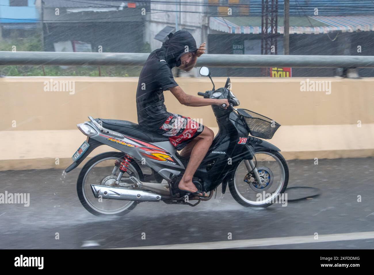 Ratchaburi, Thailand, NOV 14 2022, A young man is riding a motorcycle, shielding his eyes from the heavy rain with his hand Stock Photo