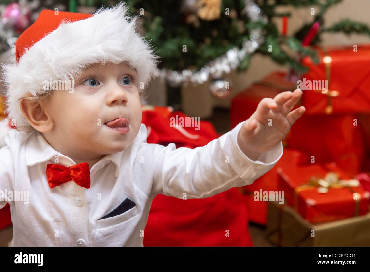 A little boy with a Santa Claus hat is raise his hand for something Stock Photo