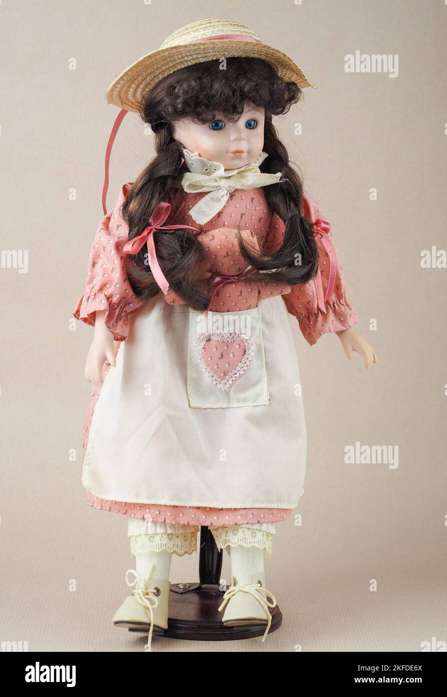 Vintage porcelain doll girl with blue eyes with brown braids in a pink dress and a white apron with a toy in the pocket and a straw pic image