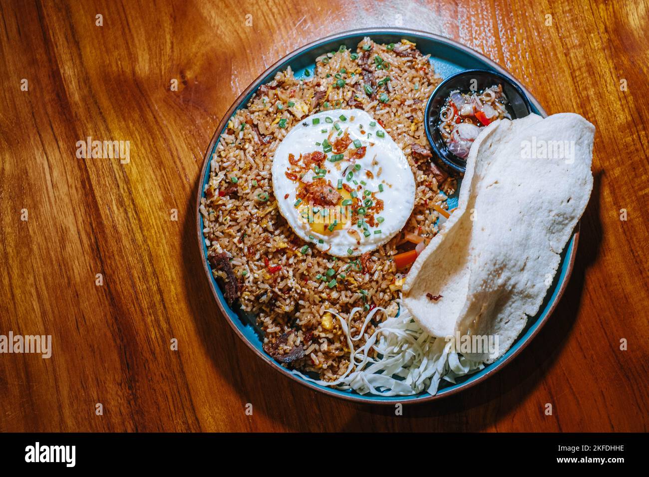 Flat lay or top view of a plate of fried rice with additional egg and typical Indonesian cracker that made from prawn in a wooden table Stock Photo