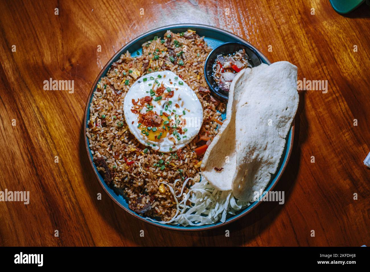 Flat lay or top view of a plate of fried rice with additional egg and typical Indonesian cracker that made from prawn in a wooden table Stock Photo